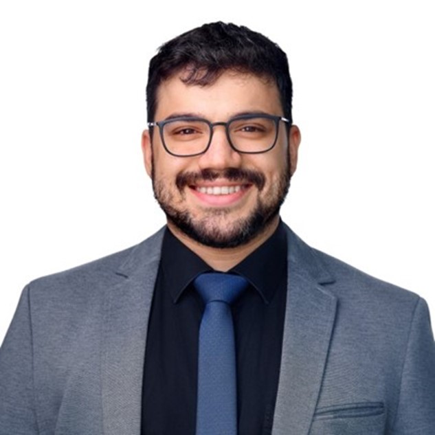 Smiling man in glasses wearing a suit and tie against a plain background.